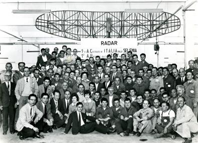 The Selenia radar design and production team. In the background, the MIM-23A HAWK anti-aircraft system produced at the  Fusaro (Naples) site and launched in 1961.